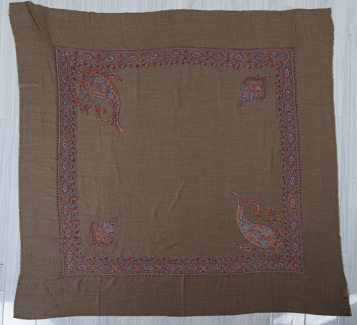 Cedar-brown square Merino wool rumal laid flat, with turquoise and copper borders, two large paisleys and two smaller corner motifs