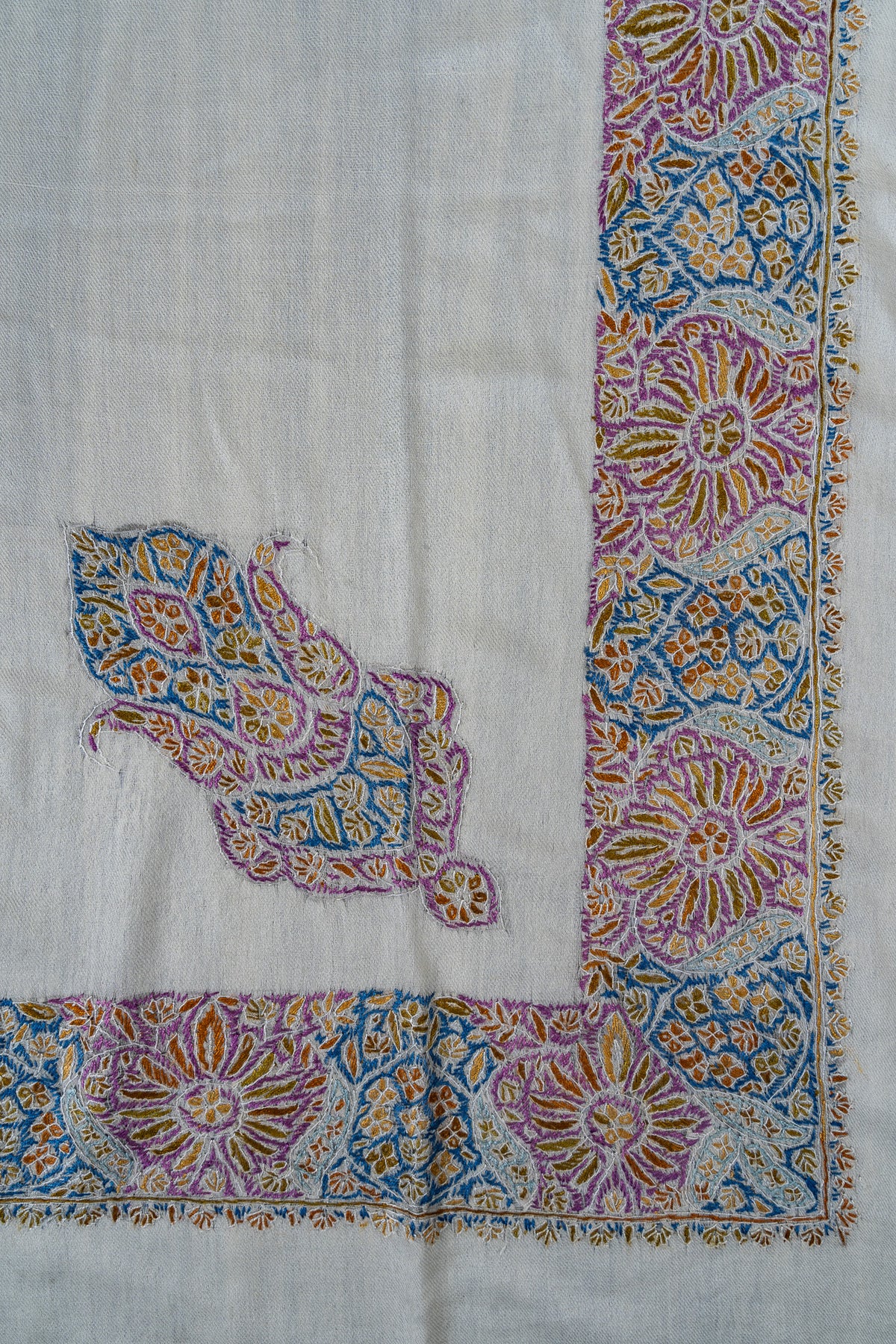 Ivory rumal corner with an elongated purple, blue and gold motif beside a wide border of flowers and leafy medallions