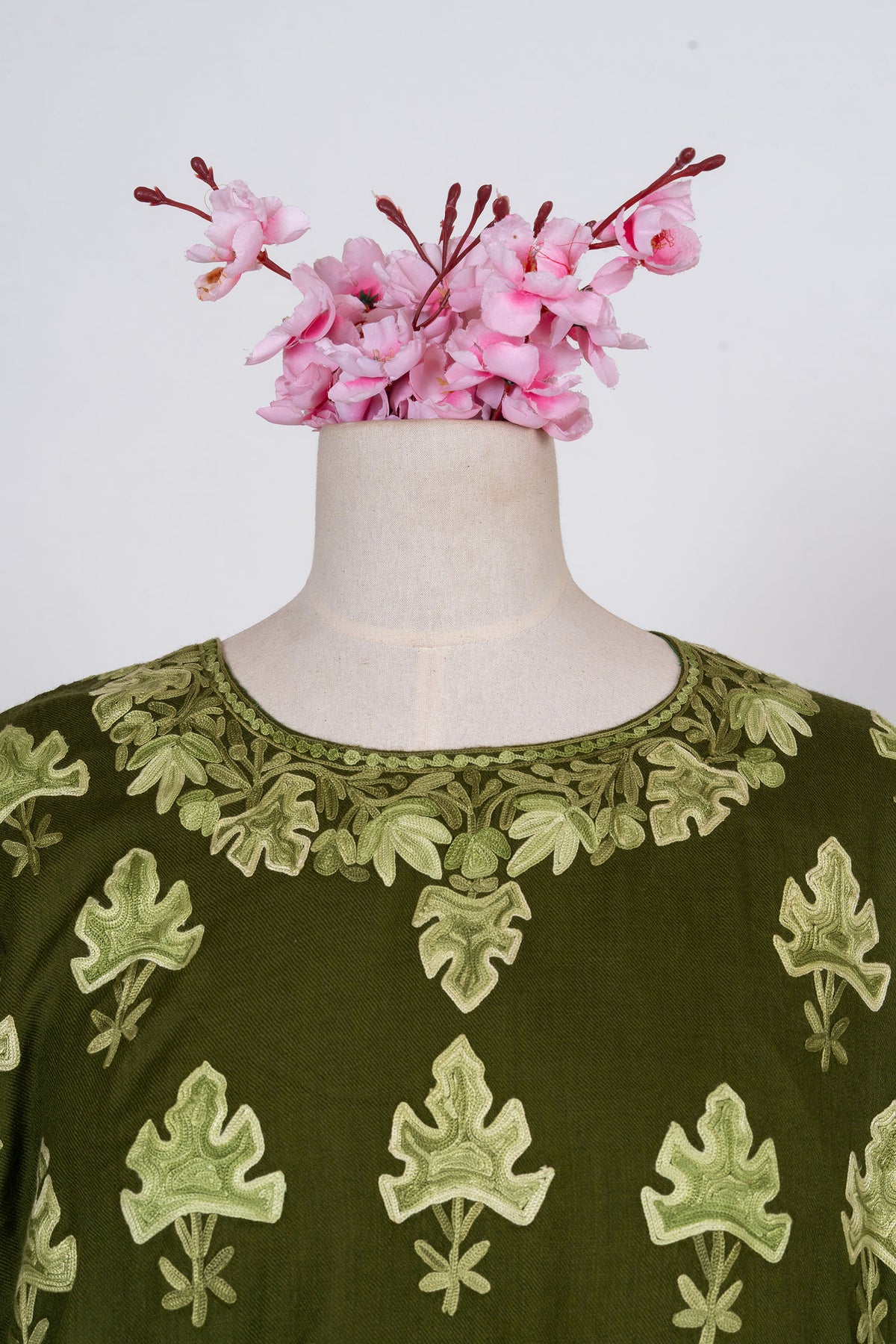 Close-up of the abaya round neckline framed by pale green leaves above scattered leaf-shaped motifs.
