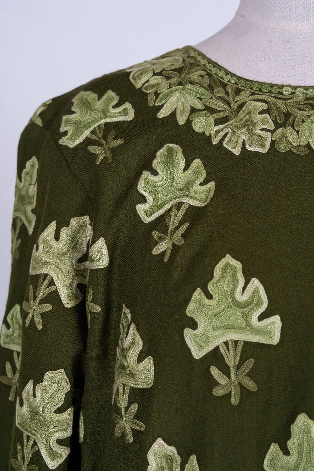 Angled neckline detail of the olive abaya with a dense leaf garland and larger leaf motifs across the chest.