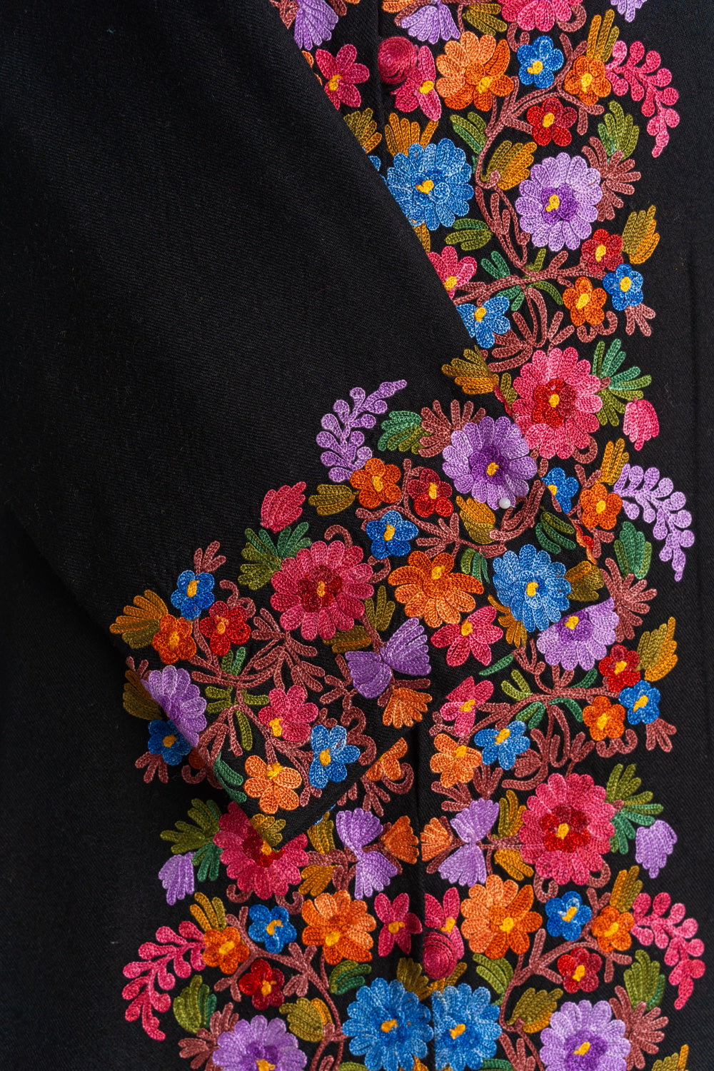Close-up of the black jacket’s crossed cuff with dense multicoloured Aari flowers beside the matching front border
