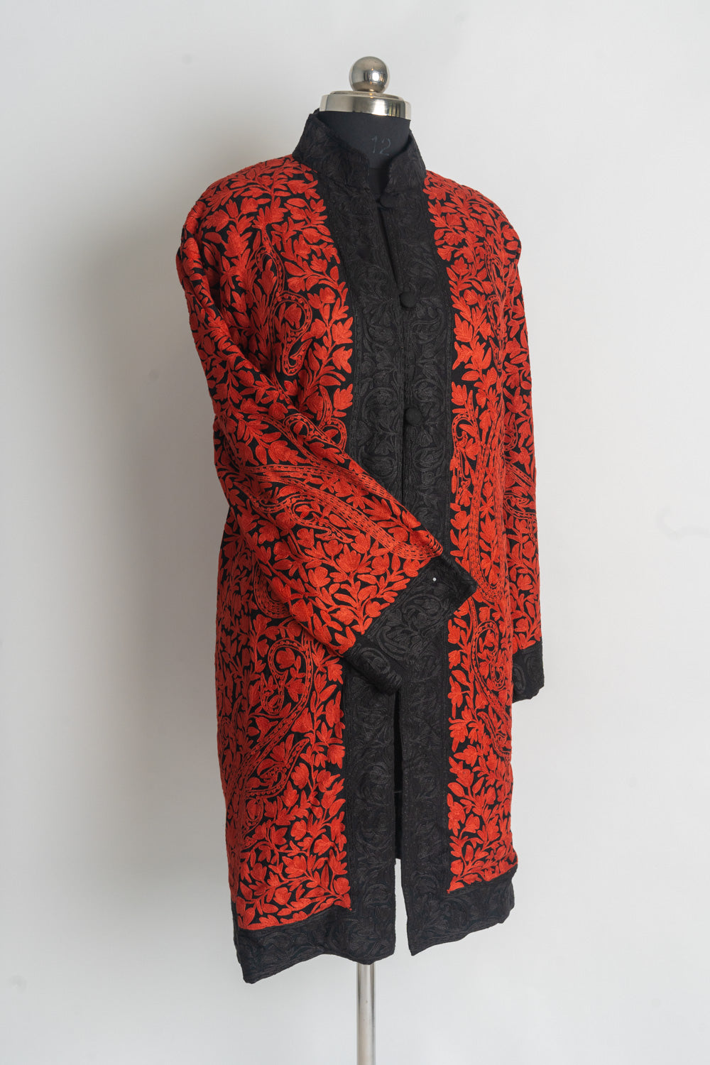 Full front view of a red-embroidered black jacket with one sleeve across the body and broad black borders at the front and hem.