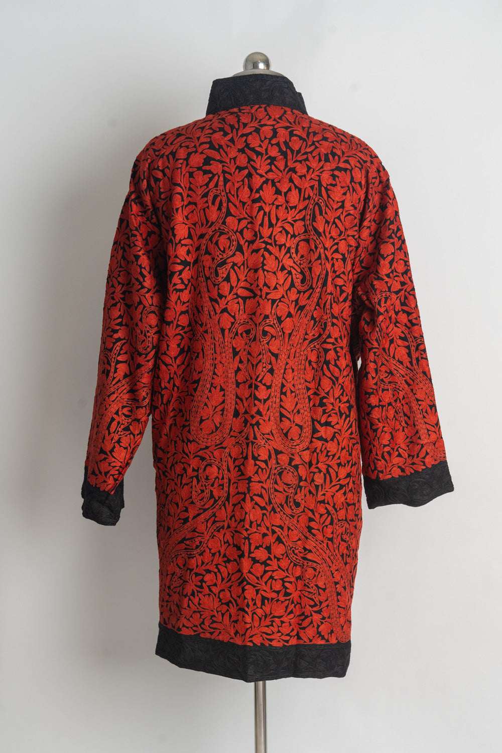 Back of a black jacket densely embroidered with red floral vines and paisleys, finished with black cuffs and hem.