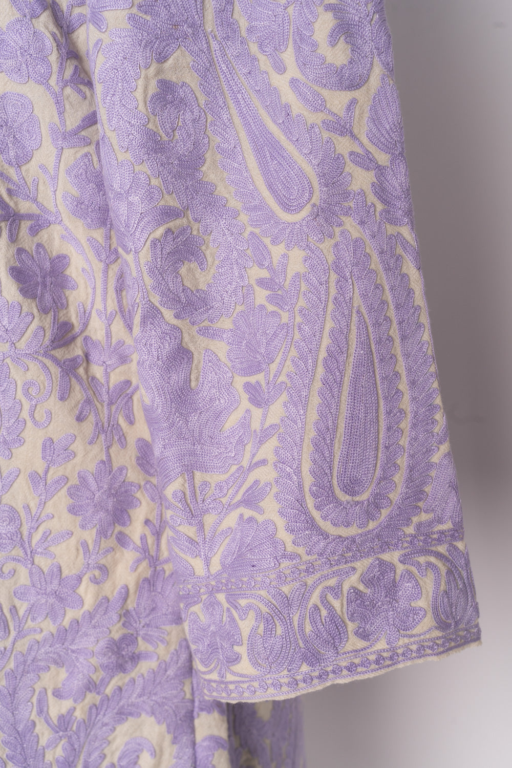 Cream jacket sleeve covered with lilac Aari paisleys and floral vines above a narrow embroidered cuff border