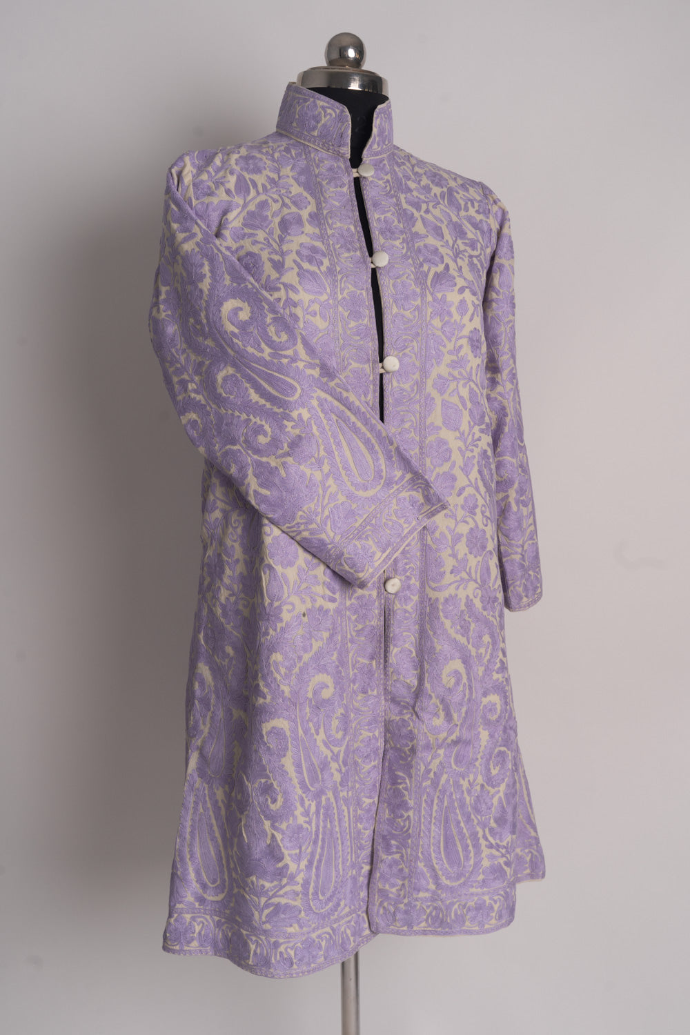 Angled full front of the cream and lilac long jacket on a mannequin, showing all-over embroidery and a crossed sleeve