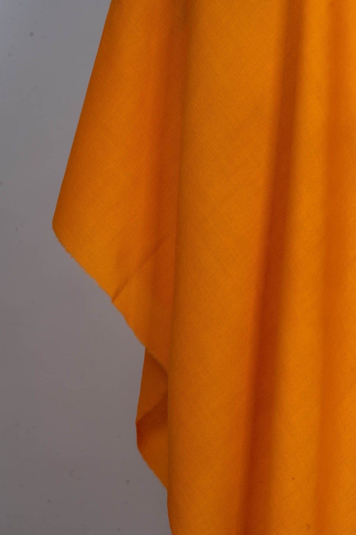 Detail of the hanging golden-yellow wrap, showing its plain edge, subtle woven texture and soft folds.