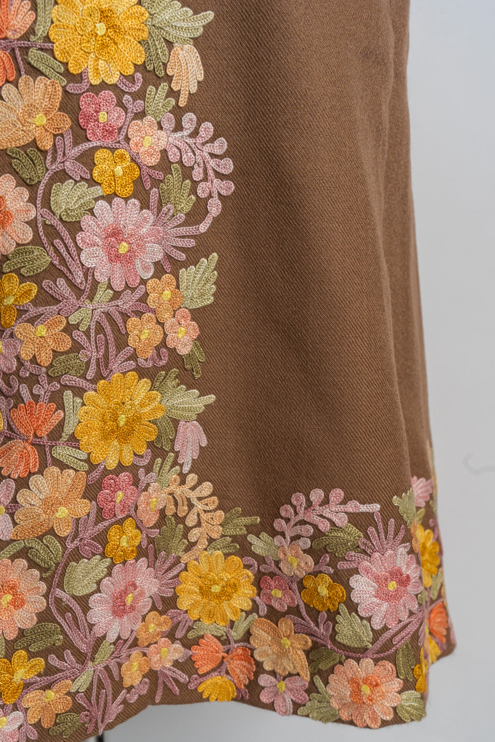 Close-up of the brown jacket’s lower front and hem with dense multicoloured Aari floral embroidery.