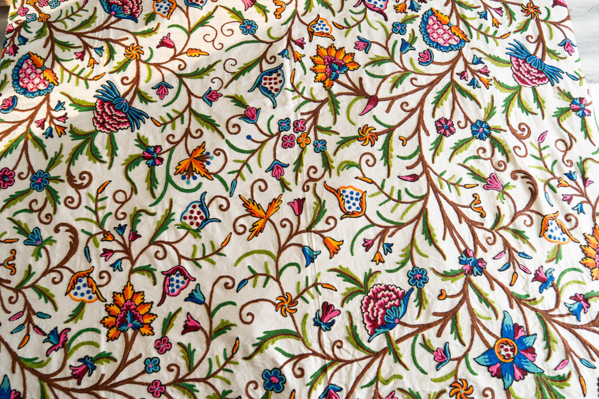 Close-up of the cream bed cover with colourful crewel flowers, green leaves and curling brown vines across the fabric.