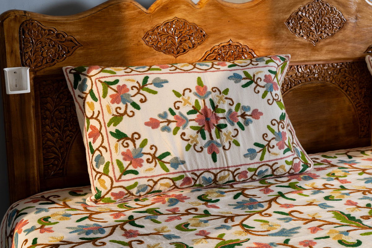 Cream cotton pillow cover with a central Crewel floral medallion and vine border, displayed on a matching embroidered bed cover