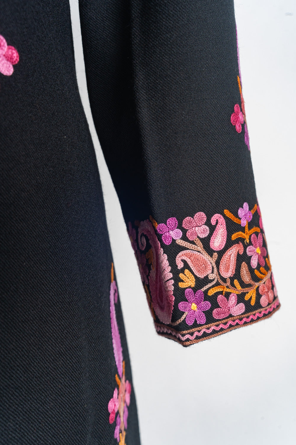 Black coat sleeve with a pink and purple floral cuff border, small paisleys and orange leafy stems