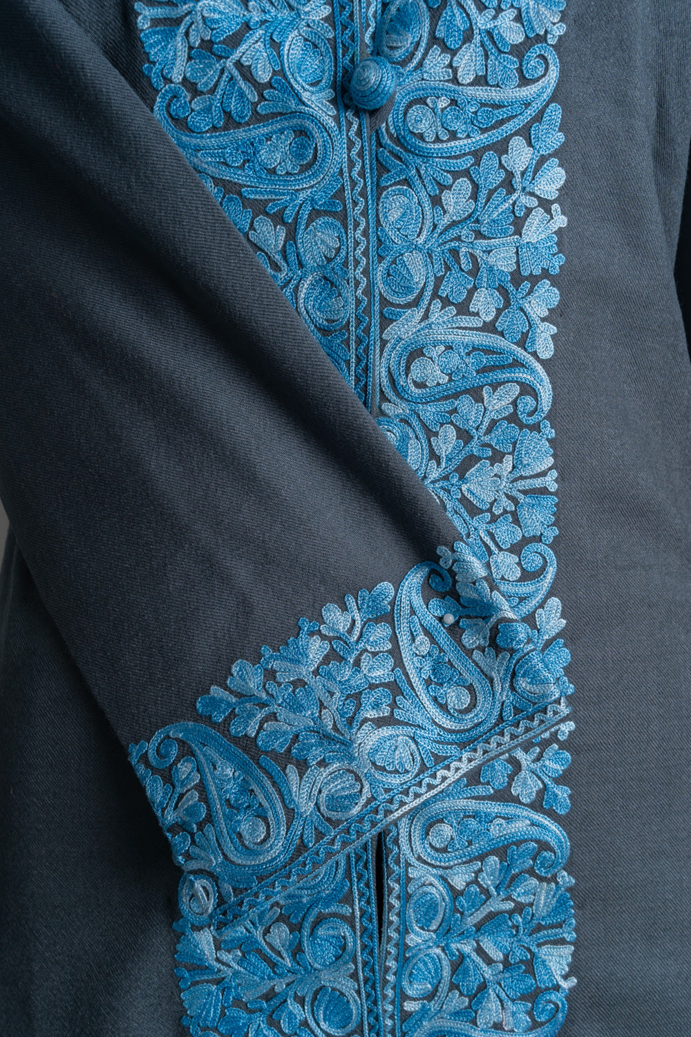 Close-up of the grey jacket’s blue embroidered cuff across its paisley-and-floral front border.