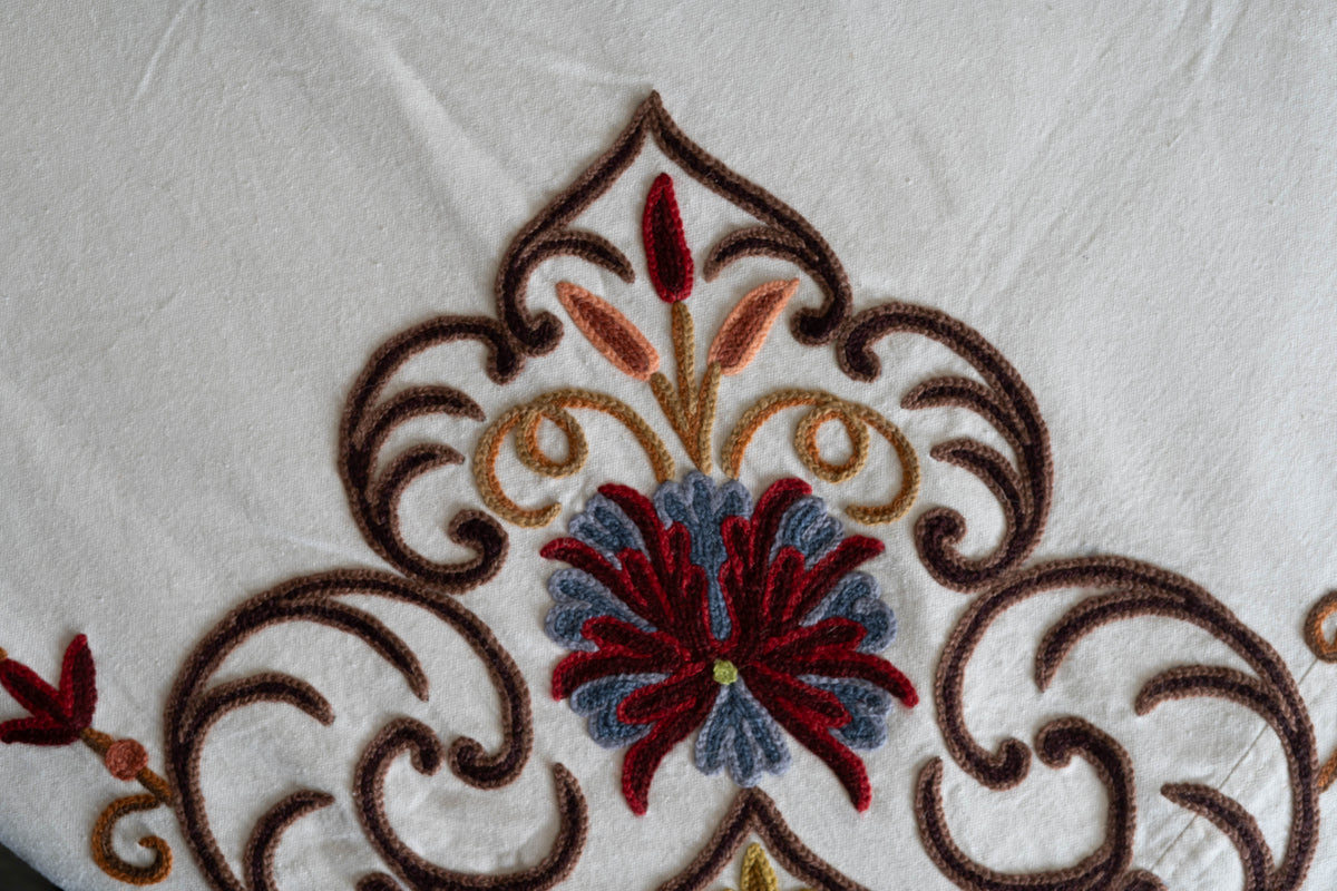 Detail of a red-and-blue embroidered flower framed by pointed brown scrollwork and small coloured leaves on the bed cover
