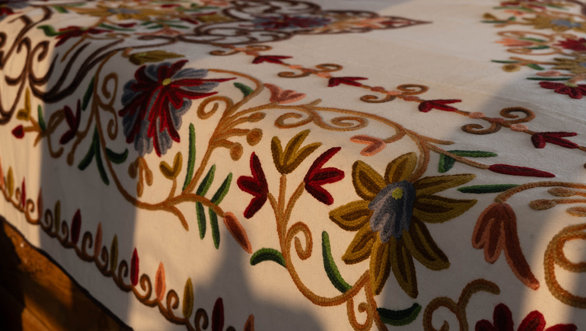 Detail of the bed cover hanging over the mattress edge, showing multicoloured flowers, leaves and brown curling stems