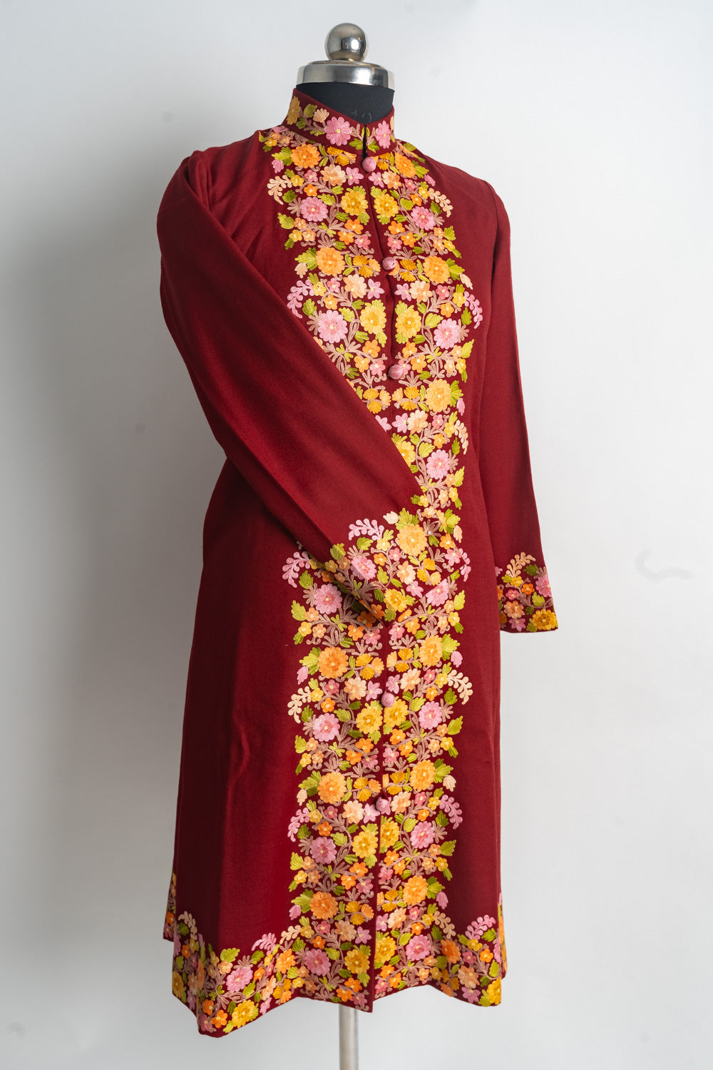 Angled full front of the ruby-red jacket with colourful floral borders and one sleeve crossed
