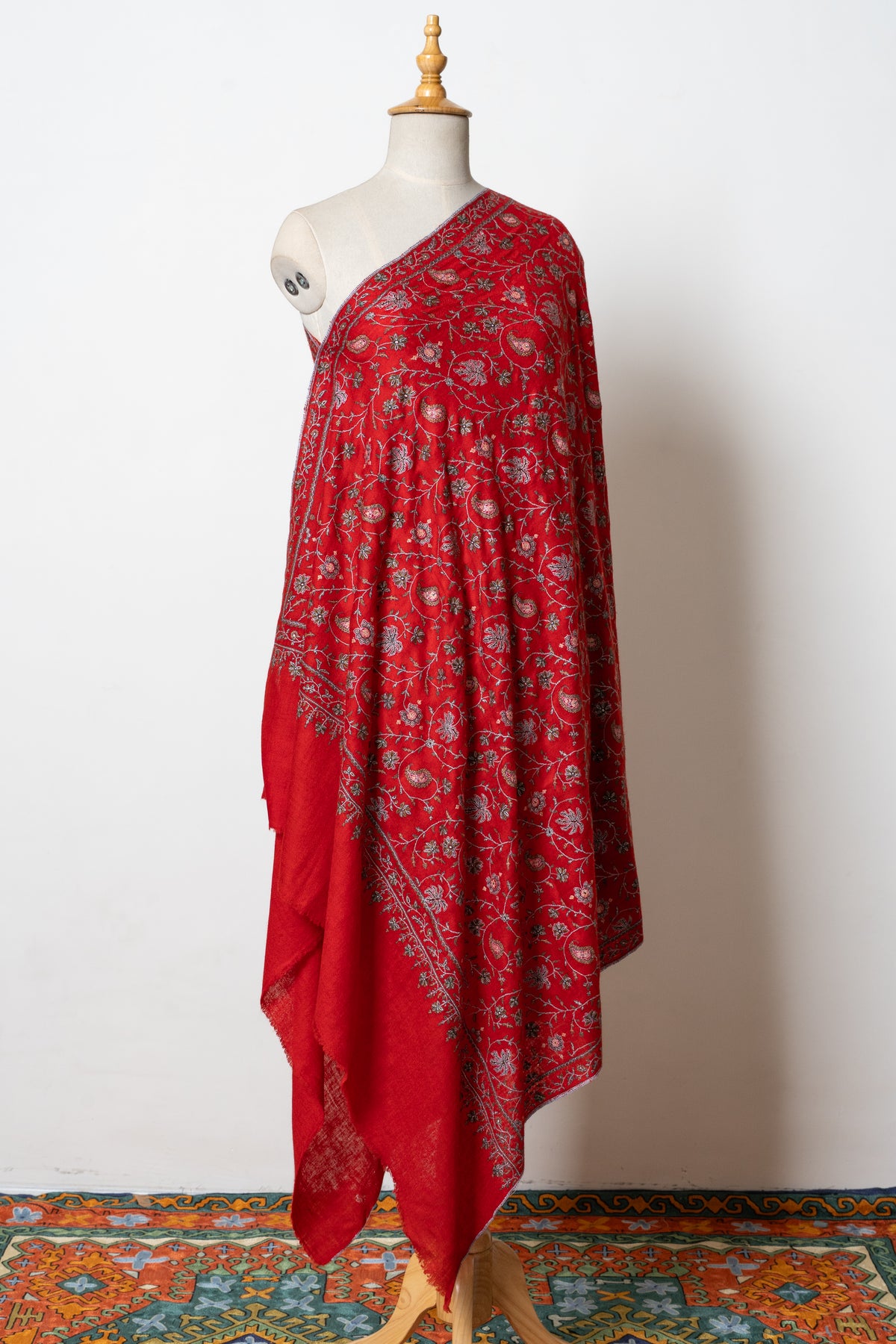 Full view of a scarlet Pashmina shawl on a mannequin, with all-over Sozni paisleys and flowers above plain red ends