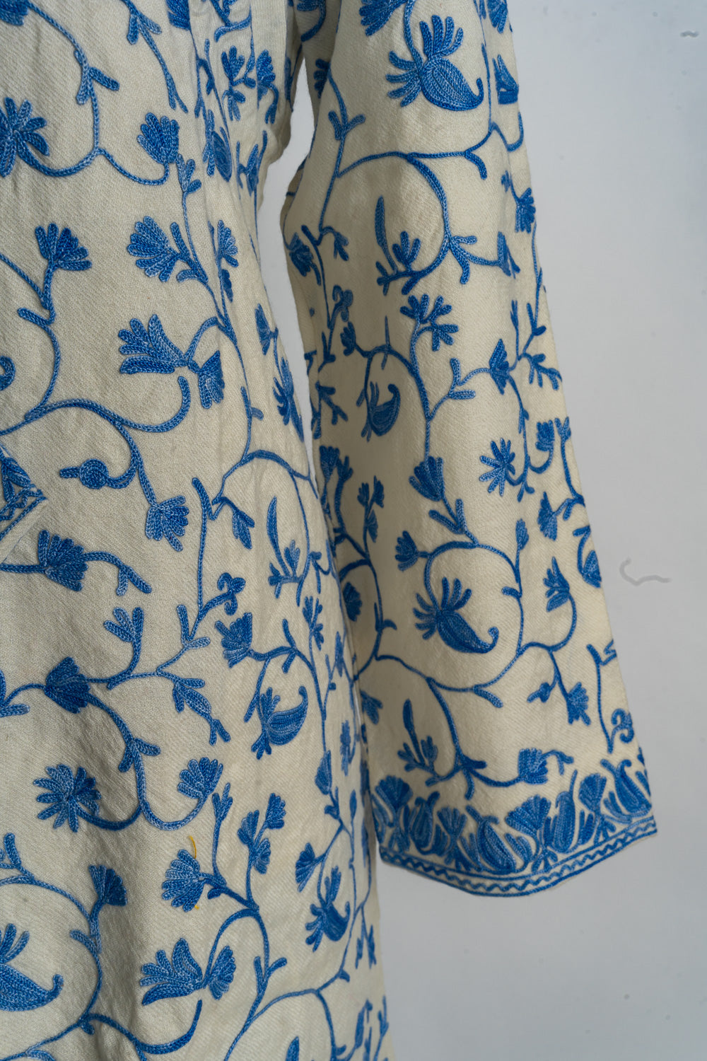Sleeve detail of the cream jacket with curling blue floral vines and a narrow patterned cuff border.