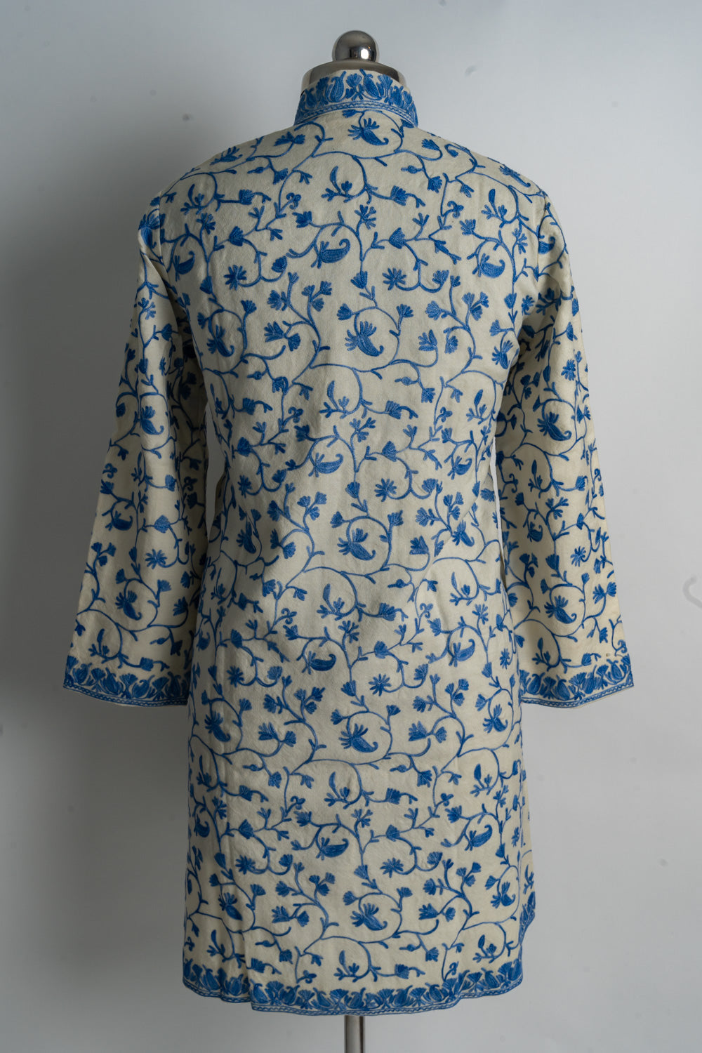 Back of a cream jacket with all-over blue floral vines and narrow embroidered cuff and hem borders.