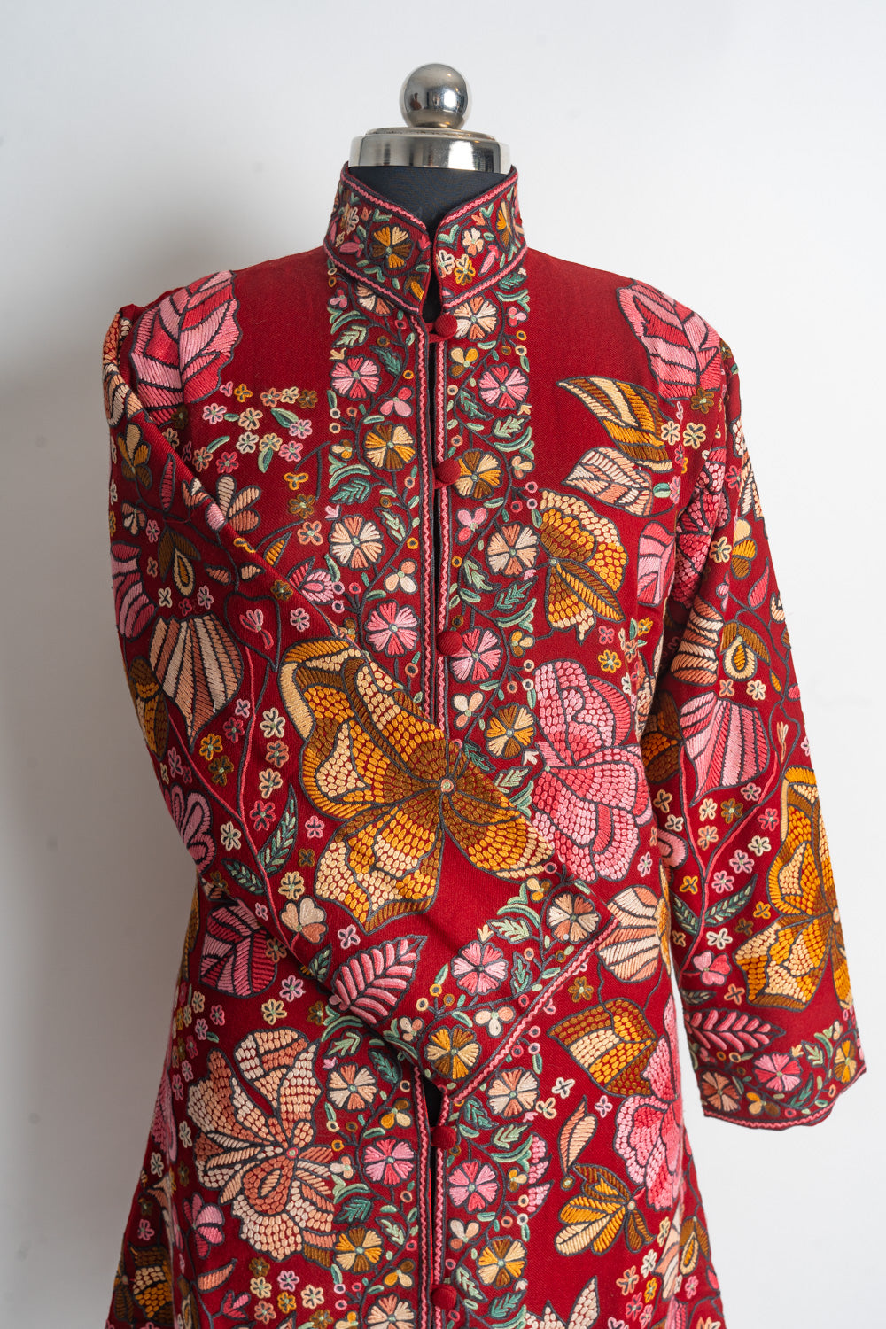 Upper front of the red Aari jacket with an embroidered stand collar, floral opening borders and one sleeve folded across.