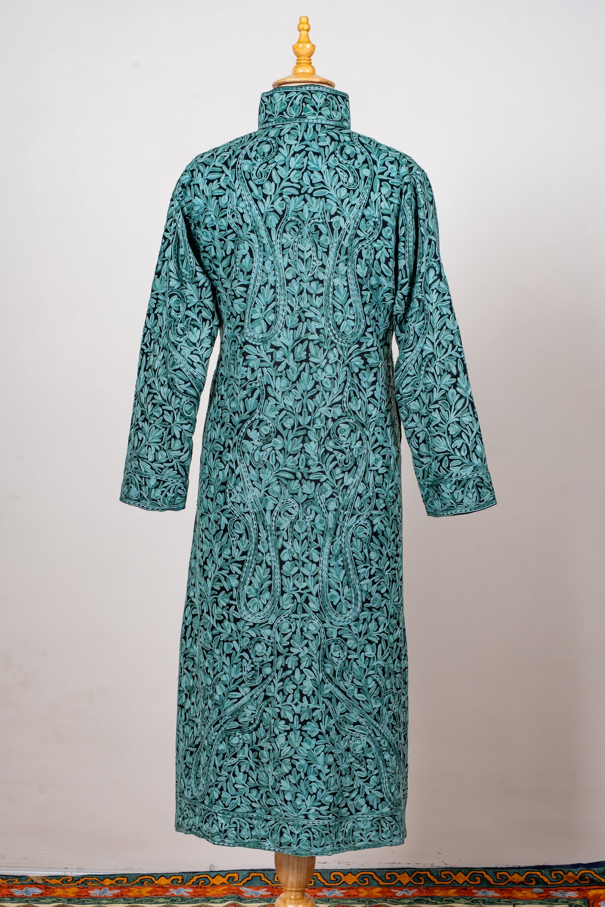 Back of a teal long jacket densely covered in turquoise Aari flowers, paisleys and leafy vines, with a high collar