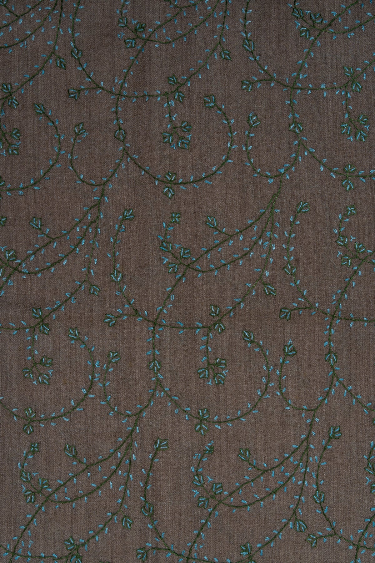 Close-up of curling dark teal Sozni stems with turquoise leaves and green clusters on taupe stole fabric