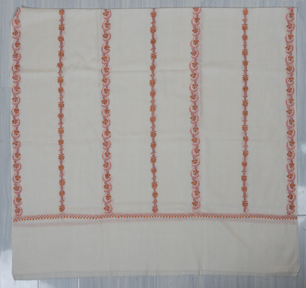 Ivory shawl laid flat with parallel pink and orange Sozni floral stripes, a narrow end border and a plain end band