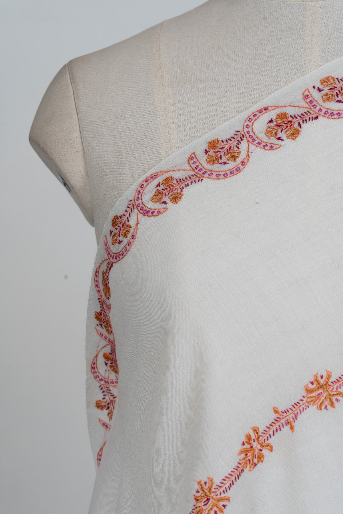 Shoulder detail of an ivory shawl showing a wavy pink Sozni stripe with orange flowers beside a finer floral row