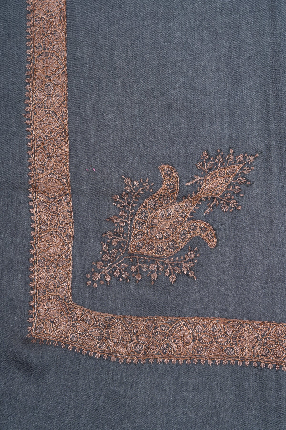 Slate-blue rumal corner with a copper and bronze Sozni motif surrounded by leafy sprays beside a narrow floral border