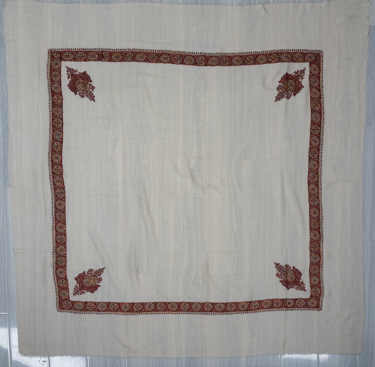 Ivory square Merino wool rumal laid flat, with a crimson and gold medallion border and four ornate floral corner motifs