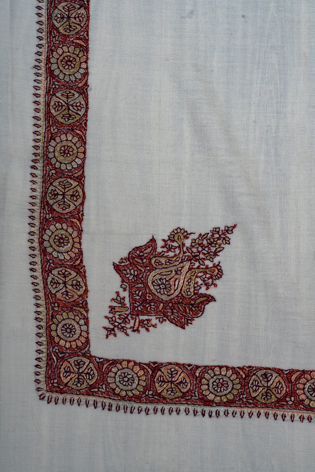 Ivory rumal corner with a crimson and antique-gold Sozni motif beside a border of alternating flower and leaf medallions