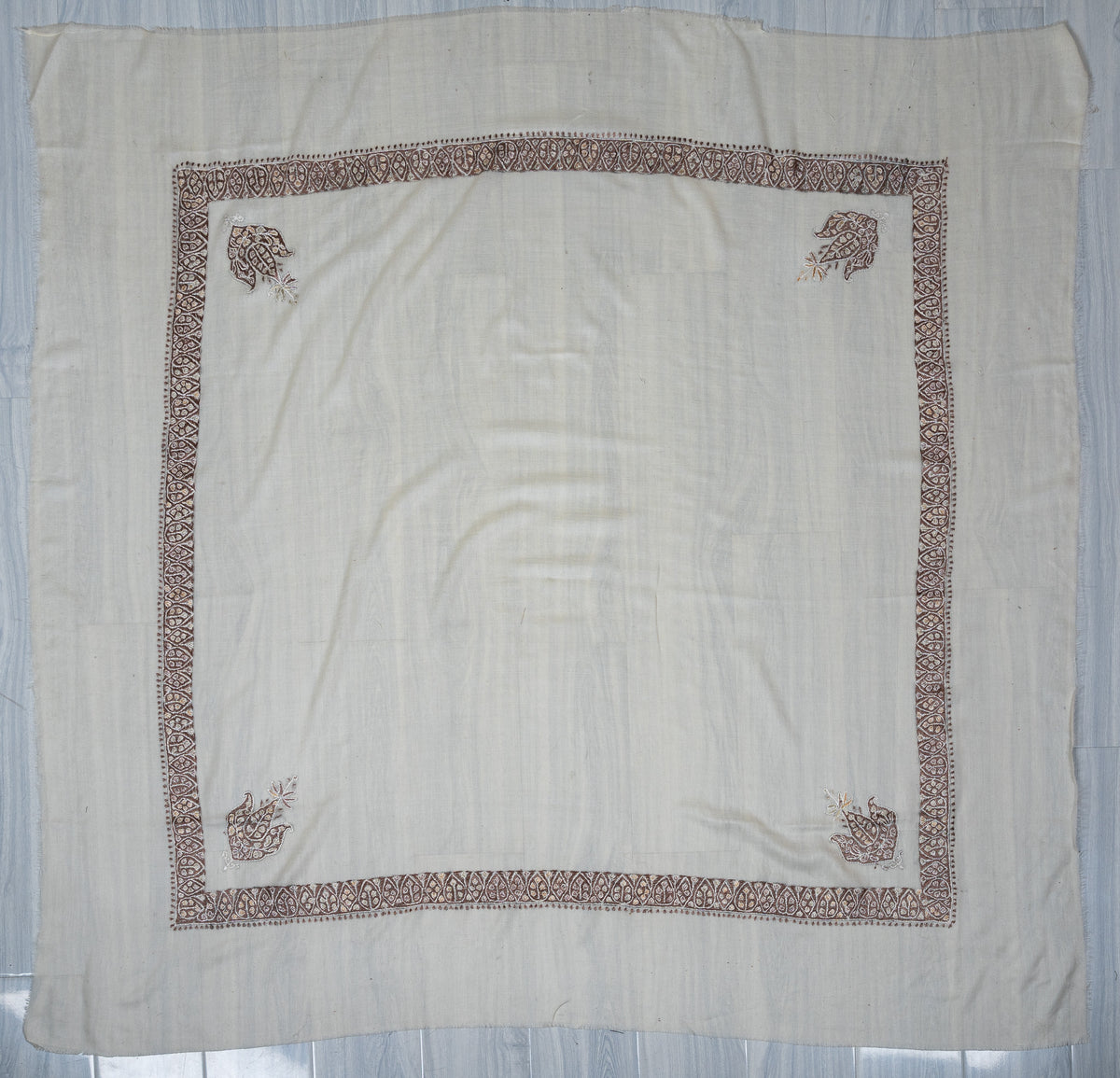 Ivory square Merino wool rumal laid flat, with a narrow mocha geometric border and four small floral corner motifs