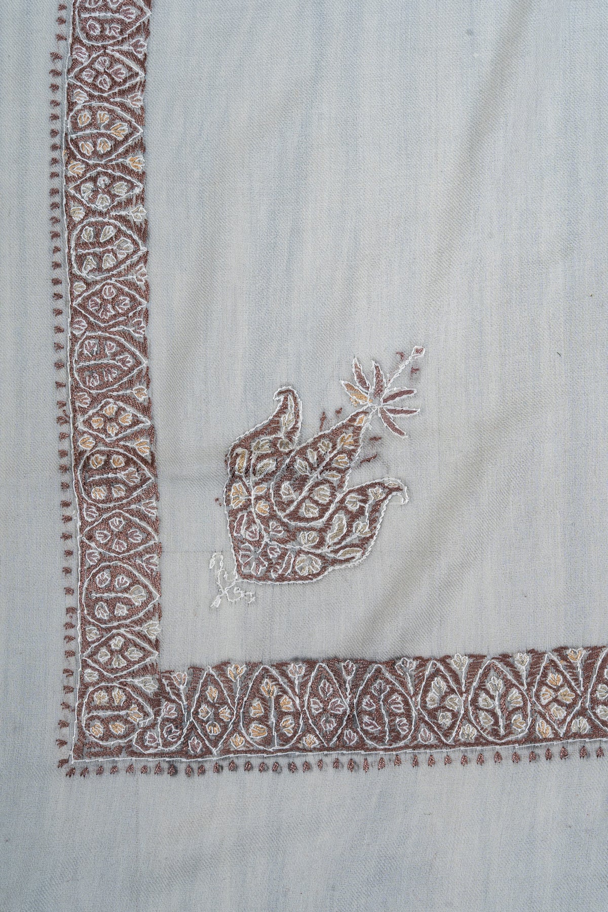Ivory rumal corner with a mocha floral motif and ivory outlines beside a narrow geometric Sozni border