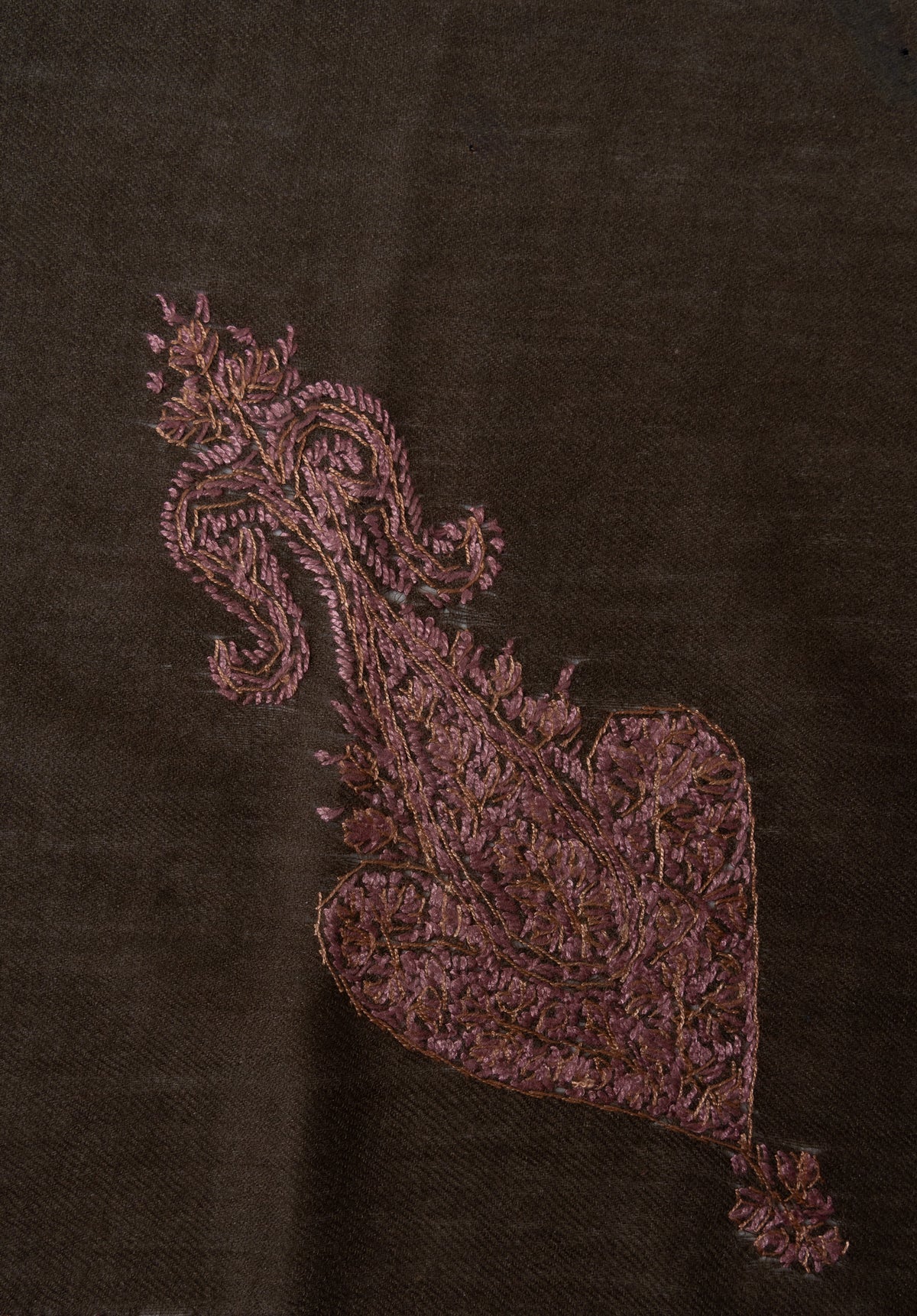 Close-up of a rose-gold Sozni paisley filled with fine floral stitching on dark brown Merino wool.