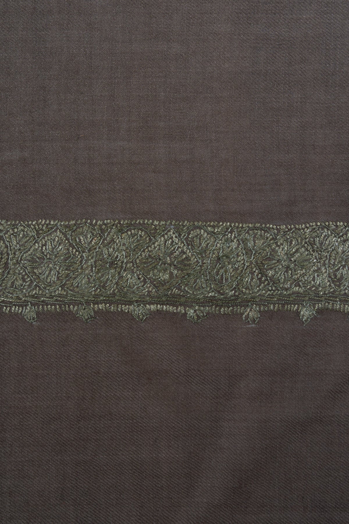 Close-up of a sage-green Sozni border densely filled with floral and leaf stitching on taupe-grey rumal fabric