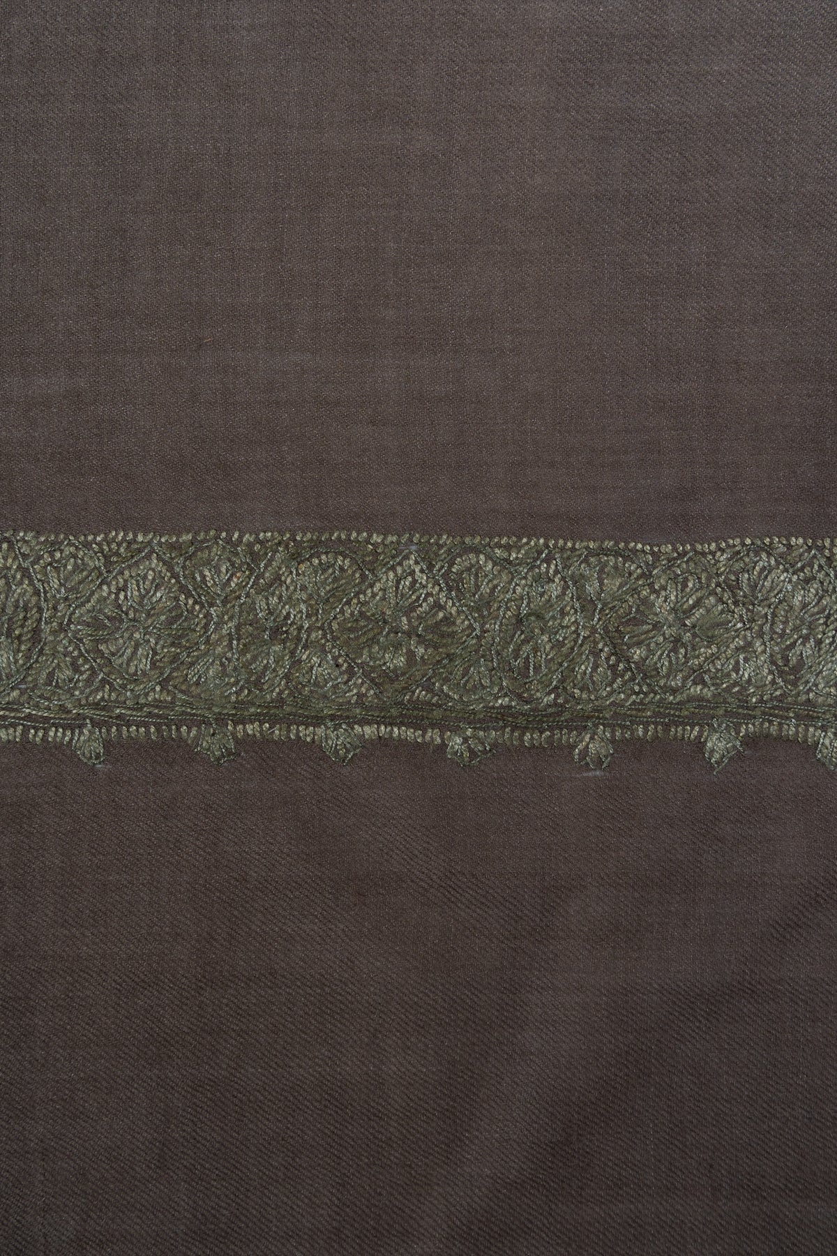 Close-up of an olive-green Sozni floral border with fine leafy edging on smoky-brown Merino wool.
