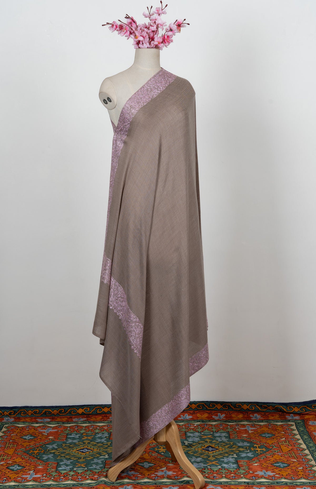 Full-length view of a taupe Merino wool shawl draped over one shoulder of a mannequin with blush-pink Sozni borders.