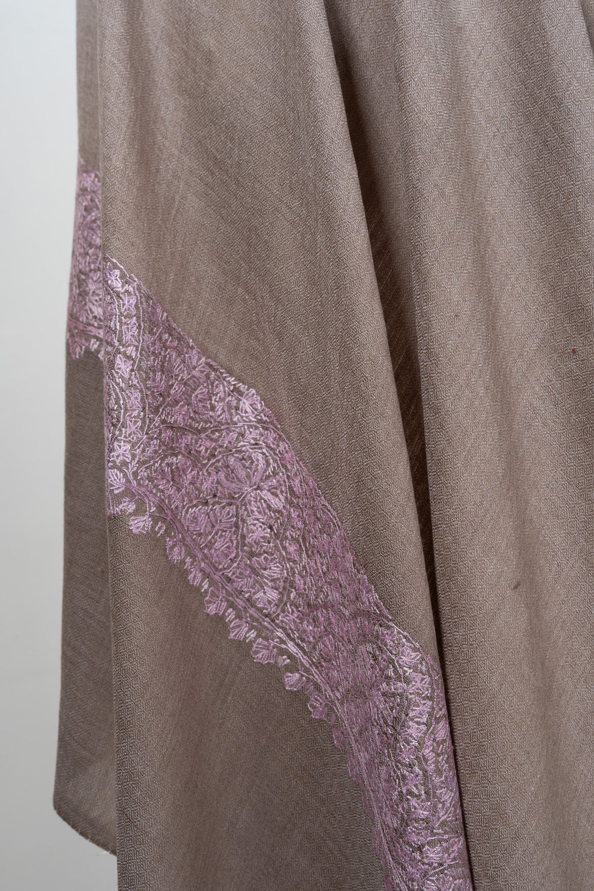 Draped folds of a taupe Merino wool shawl with blush-pink Sozni floral embroidery along the edge.