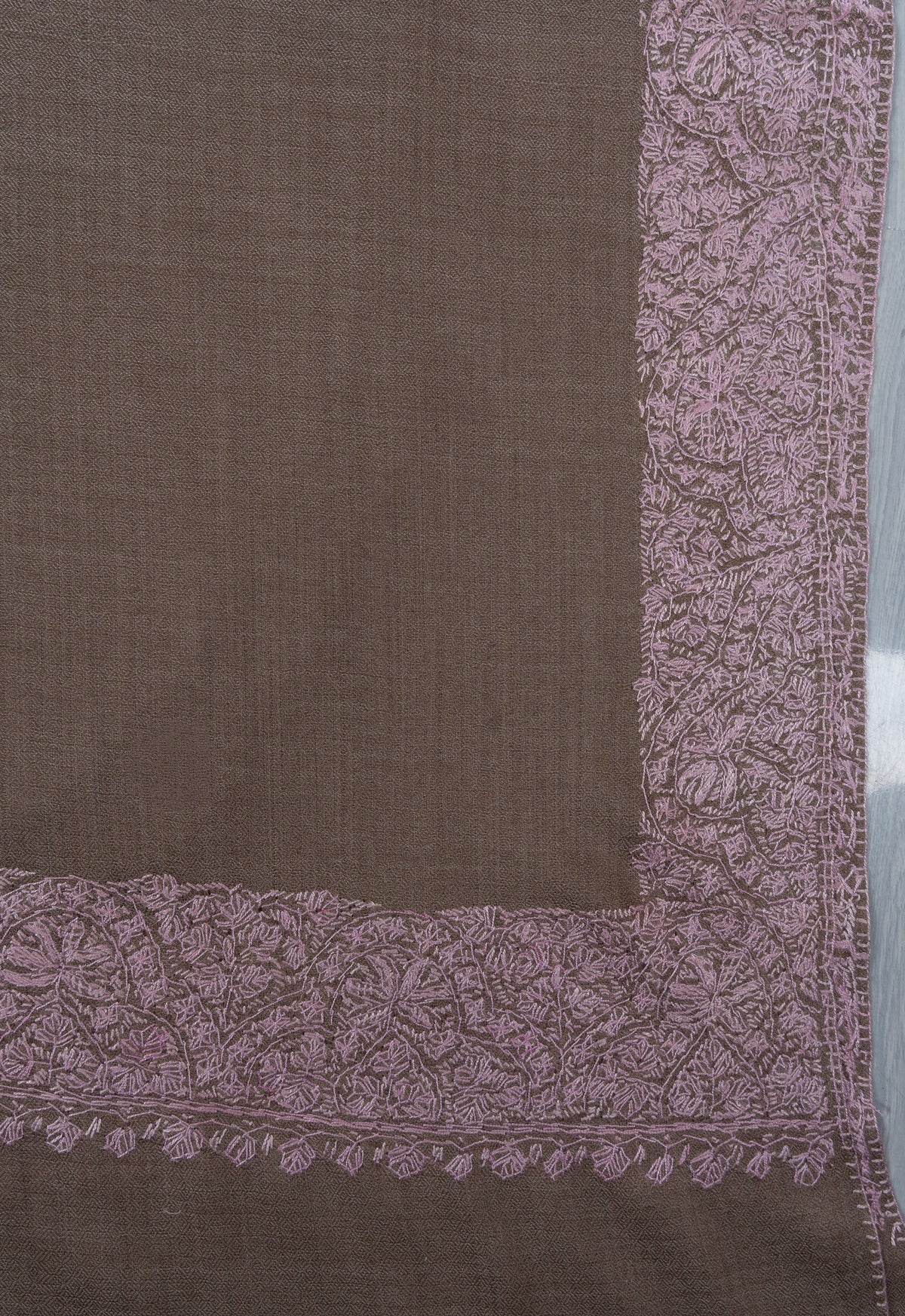 Corner of a taupe Merino wool shawl with a blush-pink Sozni floral border and small leaves along the end.