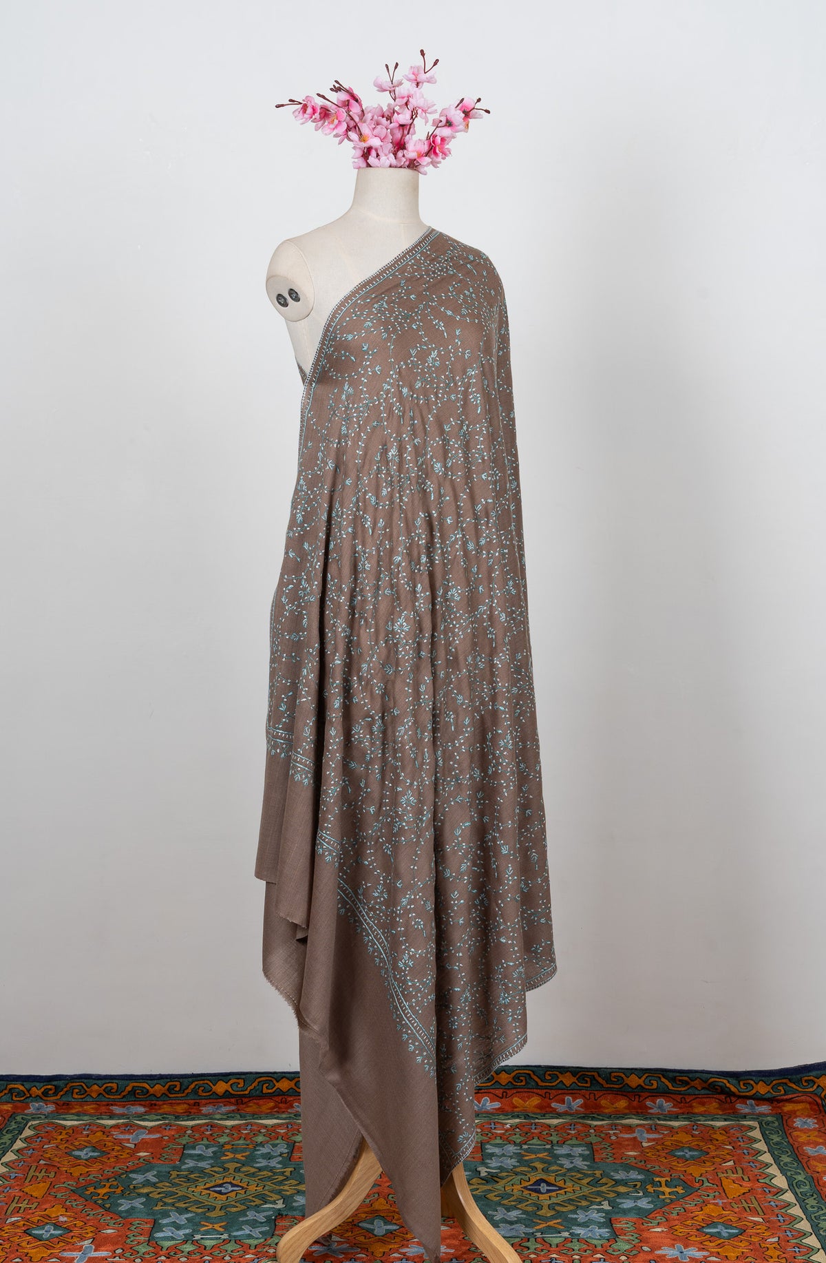 Full-length cocoa-brown shawl on a mannequin with pale aqua Sozni vines across the body and a plain end band