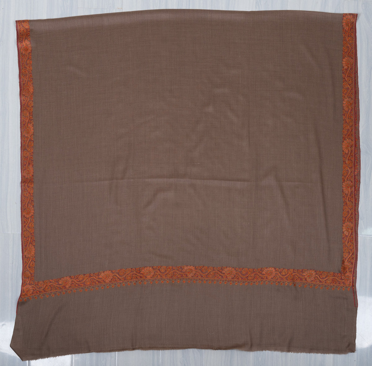 Truffle-brown Merino wool shawl laid flat, with rust-orange floral borders framing a plain field