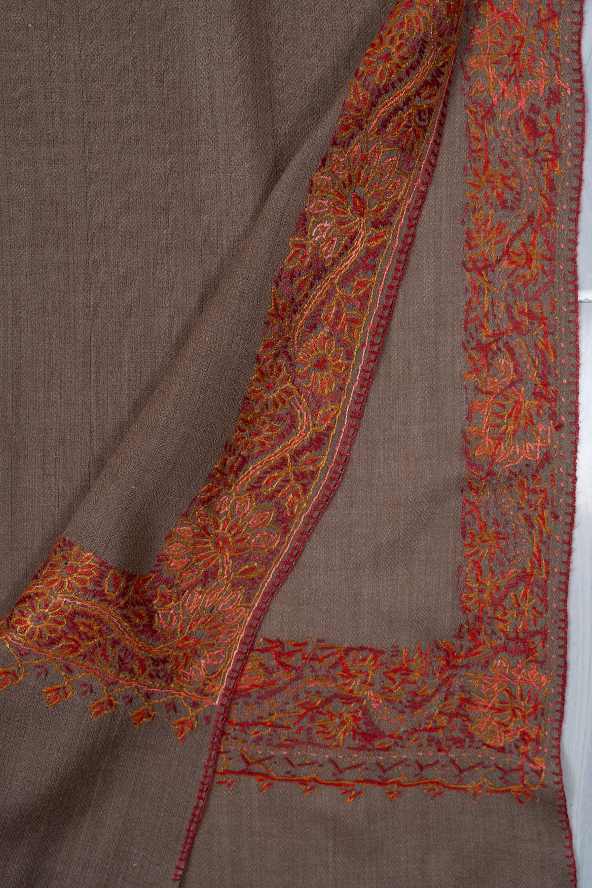 Overlapping truffle-brown shawl corners showing the front and reverse of the rust-orange embroidery