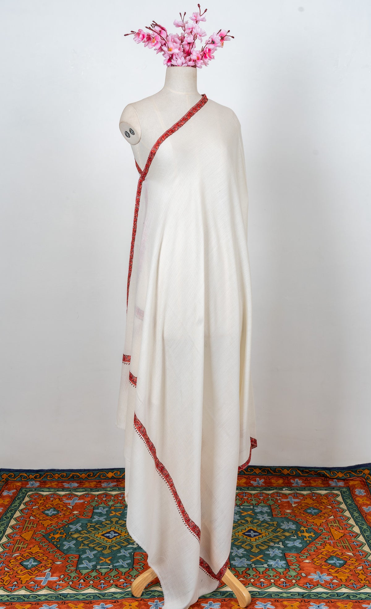 Full-length ivory shawl on a mannequin with a plain body and narrow ember-red Sozni borders