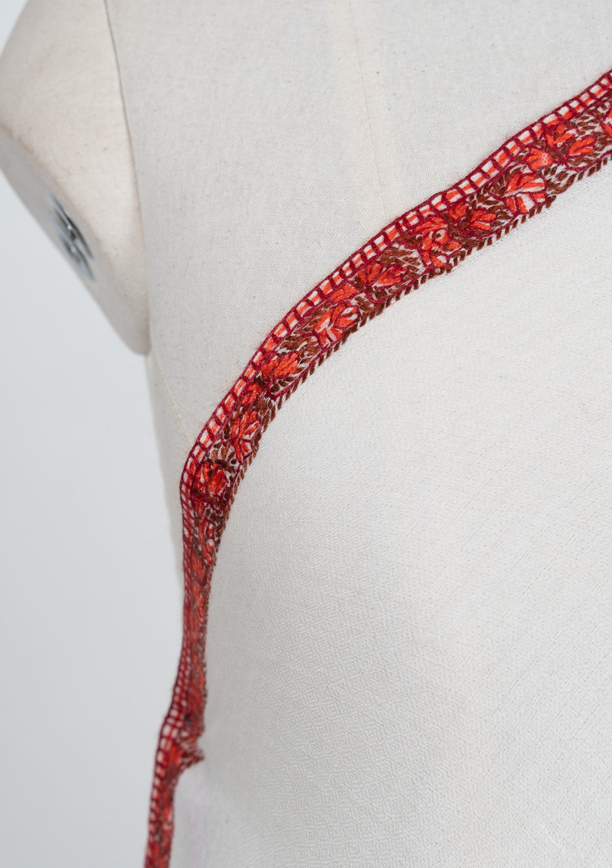 Shoulder detail of an ivory shawl showing fine ember-red Sozni floral stitching along a narrow edge