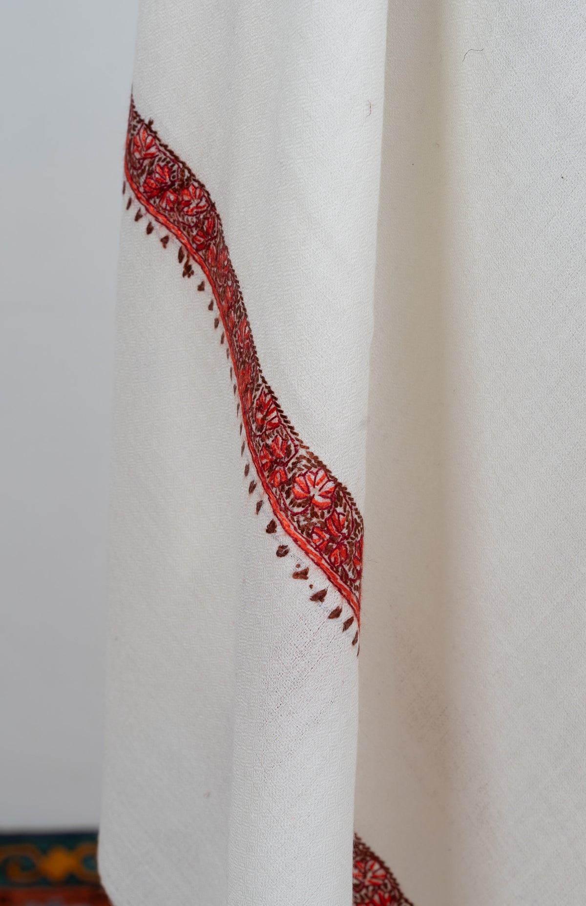 Hanging end of an ivory shawl showing a narrow red Sozni floral border and small leaf edging