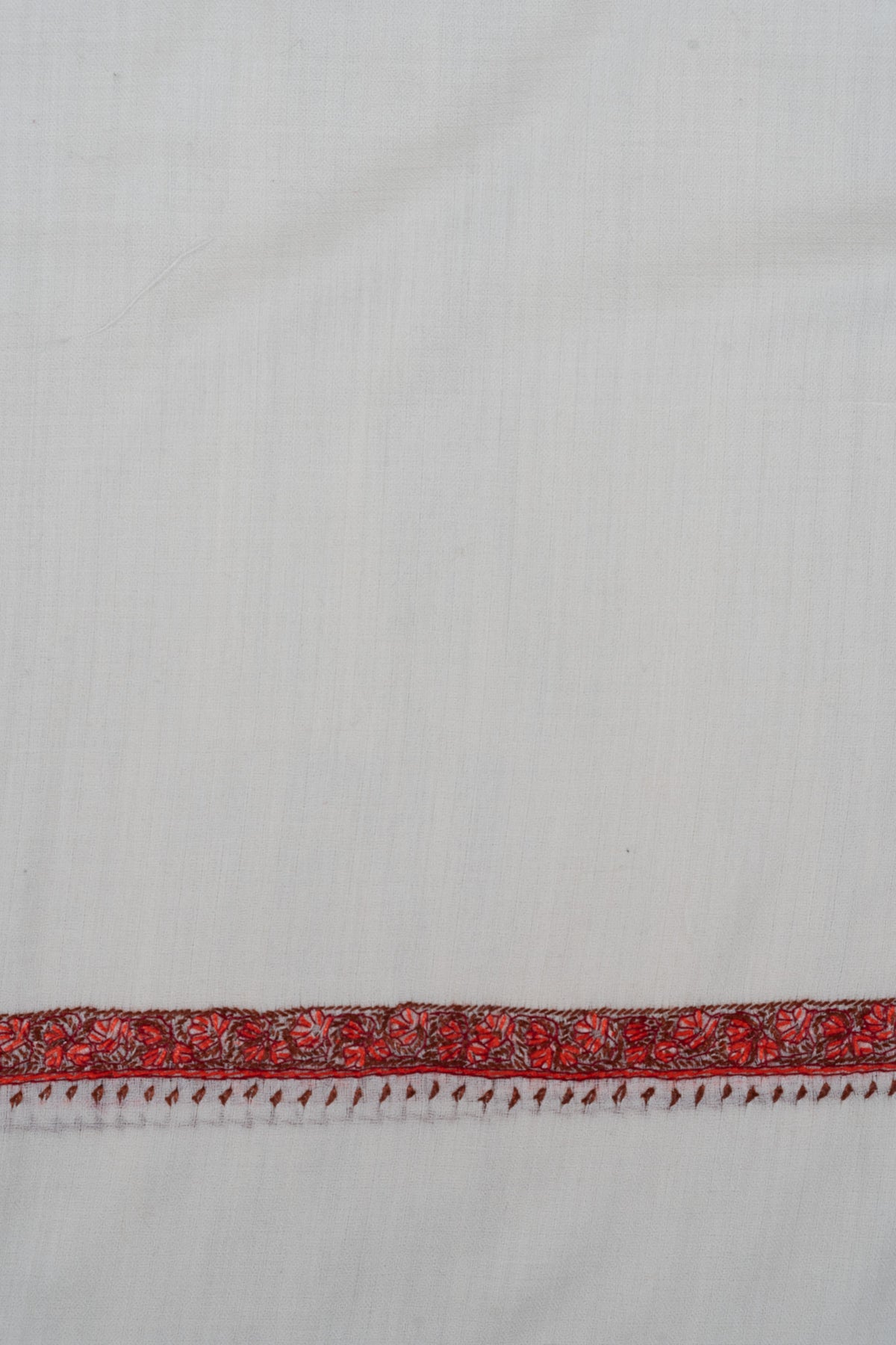 Close-up of a narrow ember-red Sozni floral border with small hanging leaf motifs on ivory shawl fabric