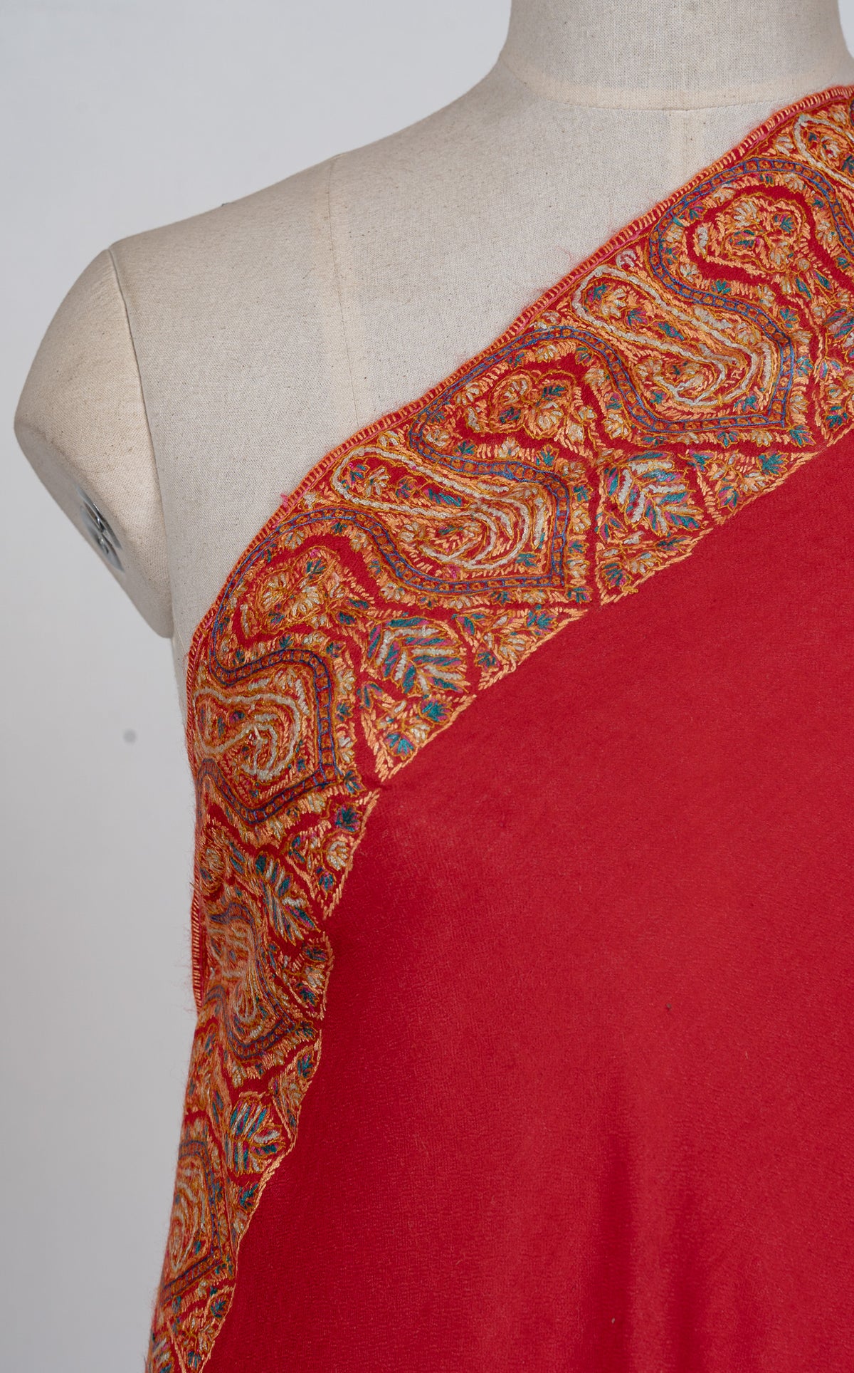 Close-up of the golden Sozni paisley border across a scarlet shawl shoulder, with blue and green accents