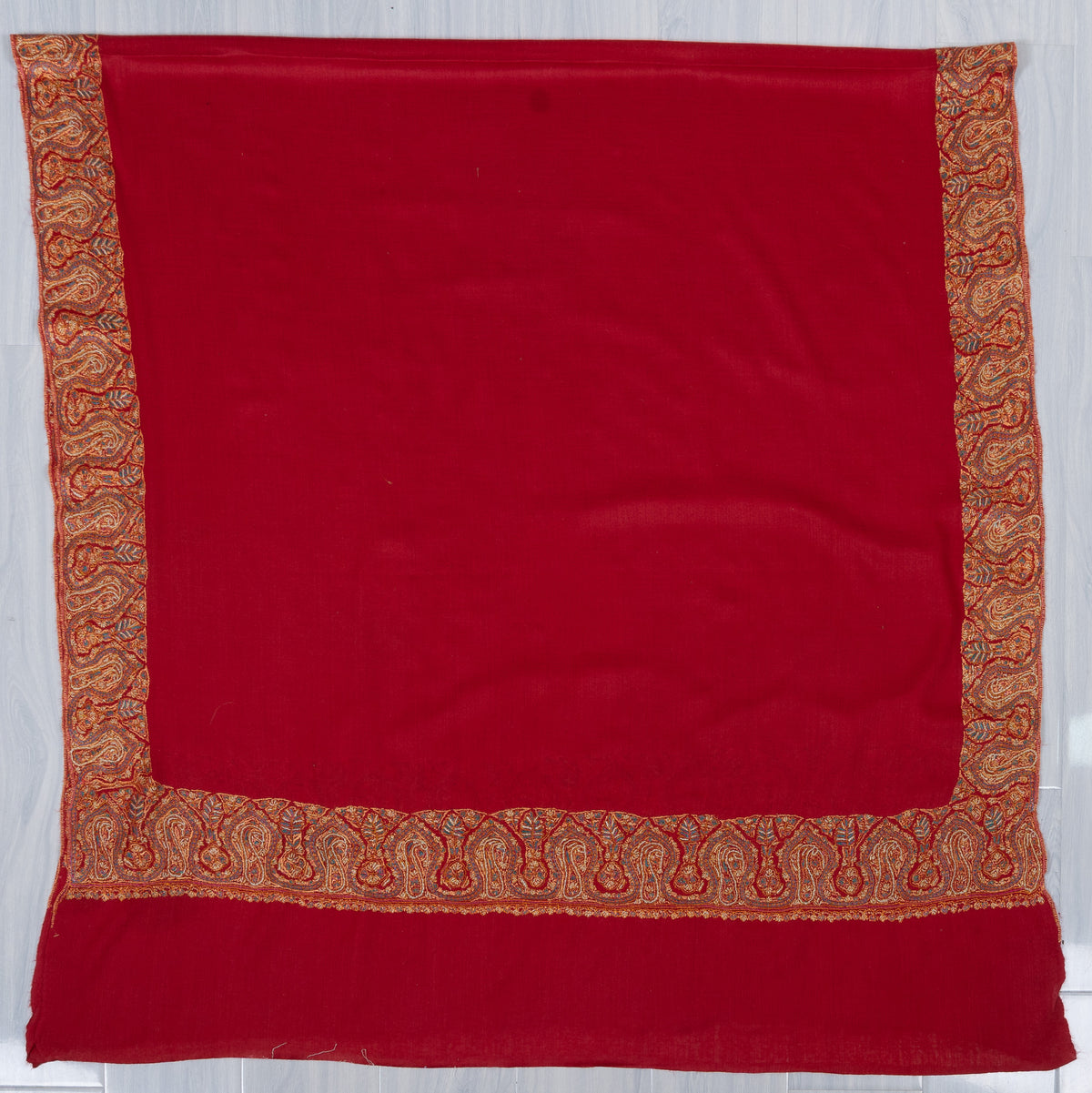 Scarlet merino wool shawl laid flat, showing a plain field framed by broad golden Sozni paisley borders