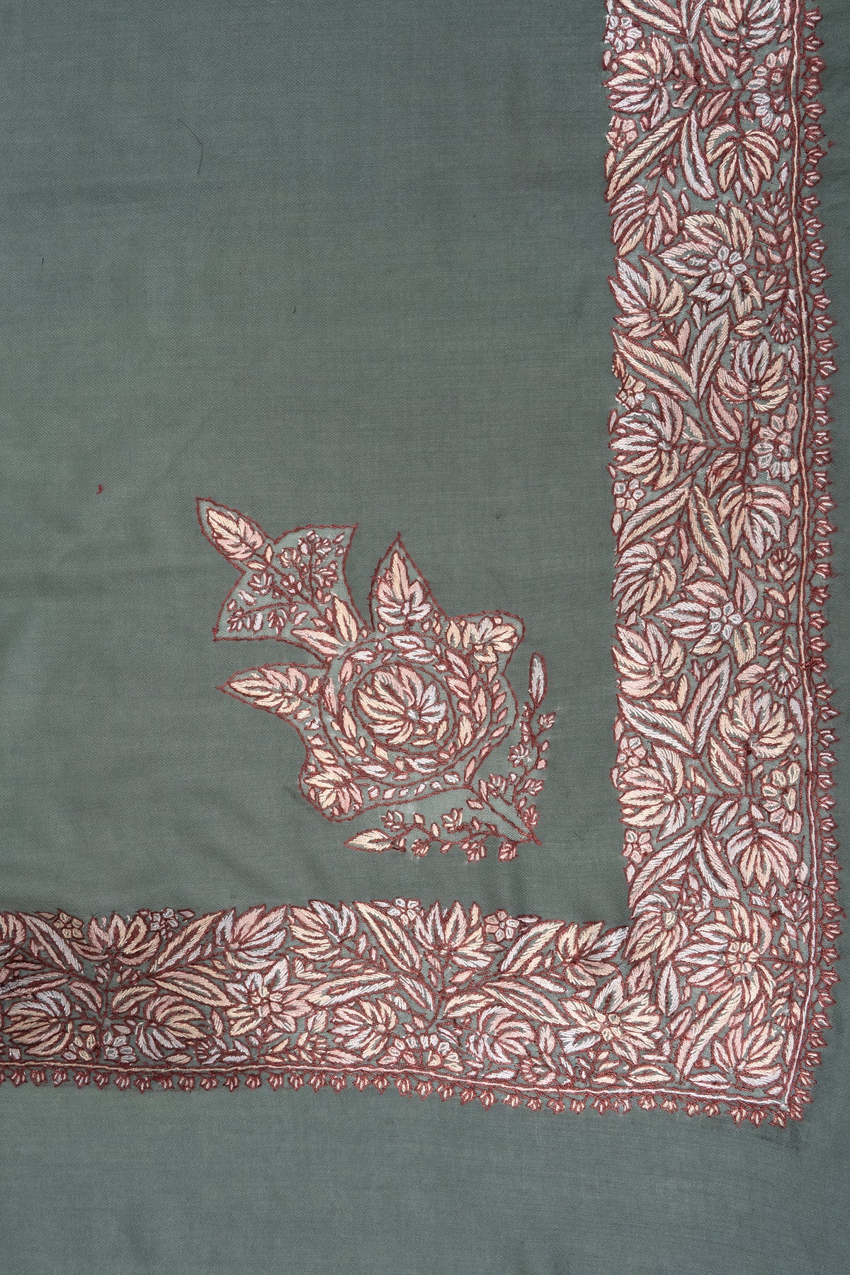 Corner detail of the green rumal showing an ornate cream and brown floral motif beside a dense embroidered border