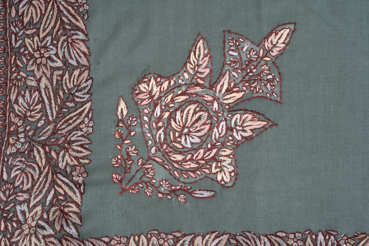 Close-up of a cream and brown floral corner motif on the sage-green rumal beside its patterned border