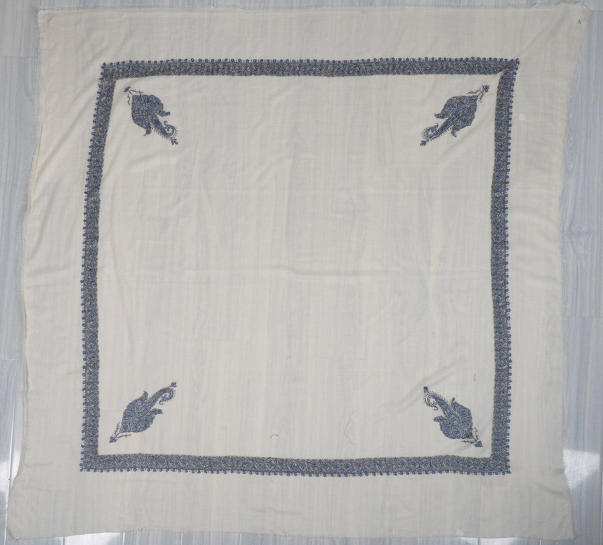 Square ivory rumal spread flat, with a narrow blue embroidered border and four blue paisley corner motifs