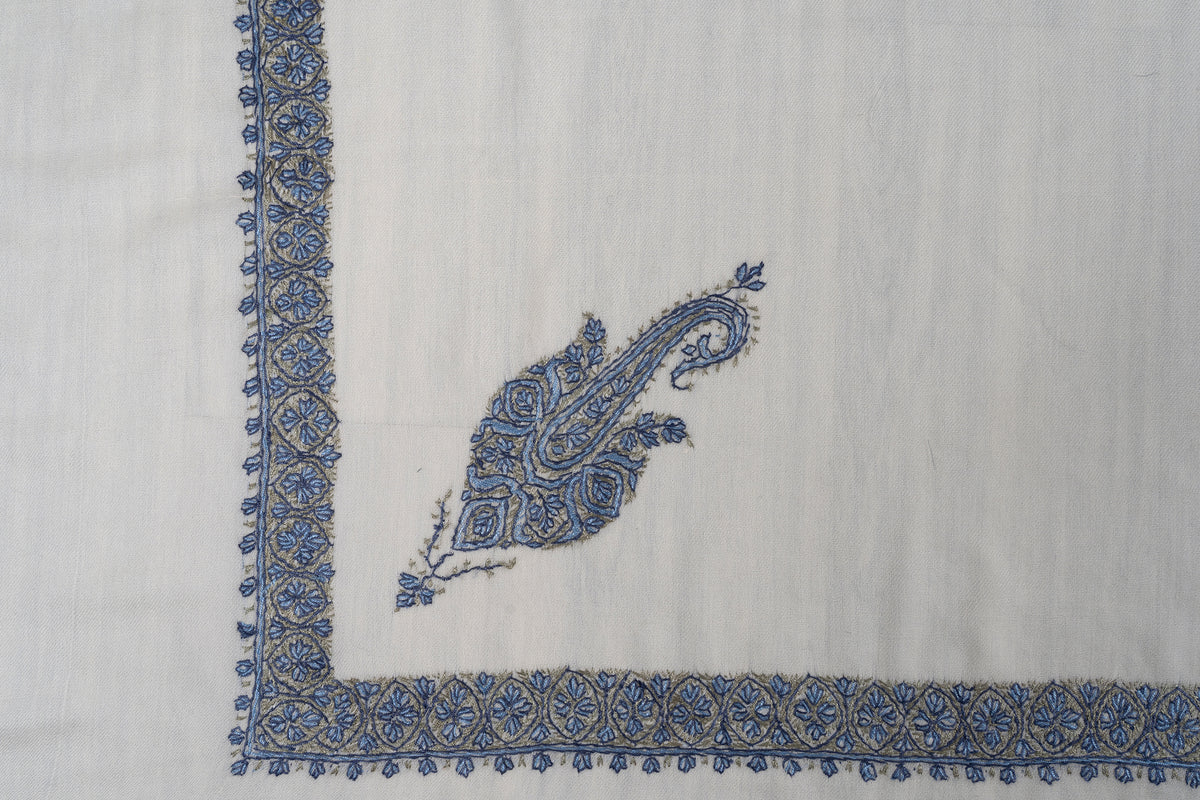 Corner detail of the ivory rumal showing a blue paisley motif above a narrow blue and muted gold floral border